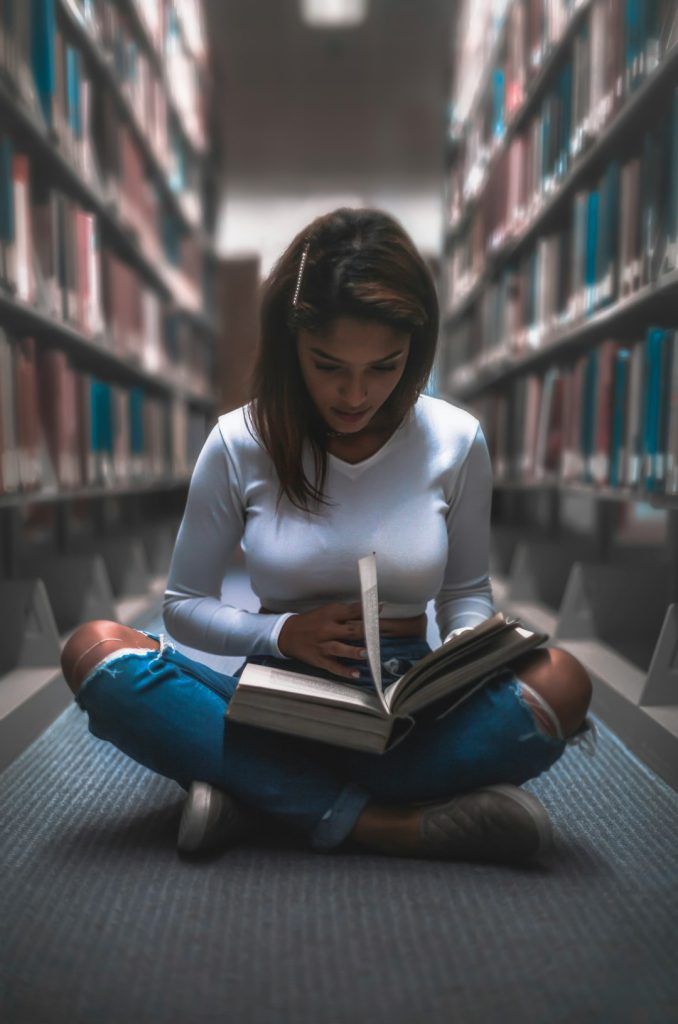 woman-sitting-between-bookshelf-6fsfv43geoo